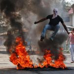 A man in a balaclava jumps over burning debris during a protest against the recent killings in Kashmir, in Srinagar